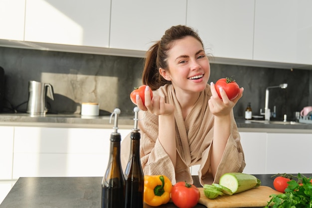 Free photo portrait of woman cooking at home in the kitchen holding tomatoes preparing delicious fresh meal