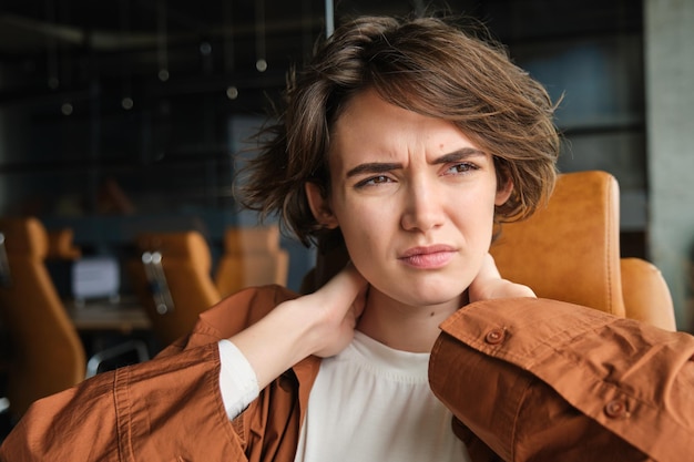 Portrait of woman feels pain in neck sits in office with laptop has tension in muscles after working