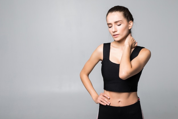 Portrait of a woman in a fitness outfit experiencing neck, shoulder and back pain isolated on white wall