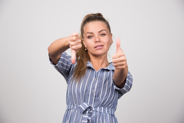 Portrait of woman giving thumbs up and down on gray wall.