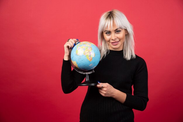 Portrait of woman holding an Earth globe on a red wall. 