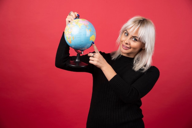 Portrait of woman holding an Earth globe on a red wall. 