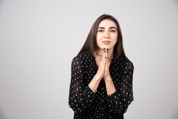 Portrait of woman holding her hands together on gray.