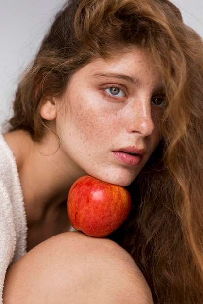 Free Photo portrait of woman holding a red apple between her face and knee