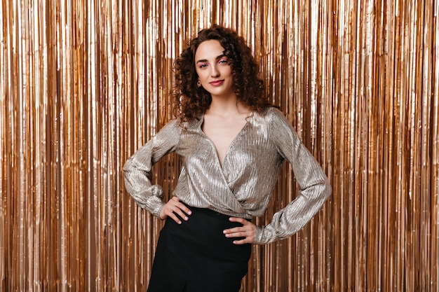 Portrait of woman in silver blouse posing on shiny background