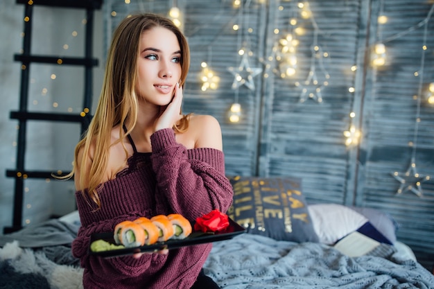 Free Photo portrait of woman sitting on bed at home, eating sushi from a black plate