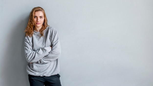 Portrait of a woman standing against grey wall with her arms crossed looking at camera