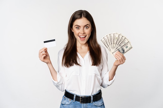 Portrait of woman standing with cash and credit card, concept of money, microcredit and loans, standing over white background happy