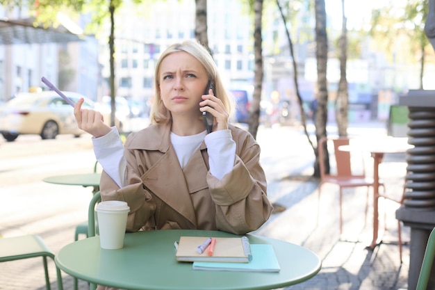 Free Photo portrait of woman student doing homework outdoors in cafe holding pen frowning while calling someone