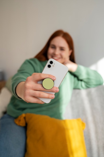 Free photo portrait of woman using her smartphone at home on couch by holding from pop socket