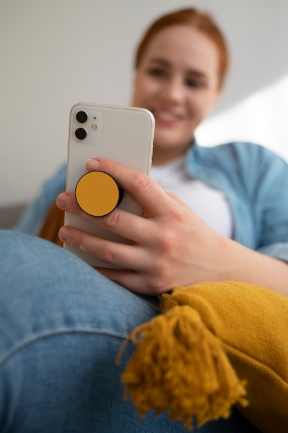 Portrait of woman using her smartphone at home on couch by holding from pop socket