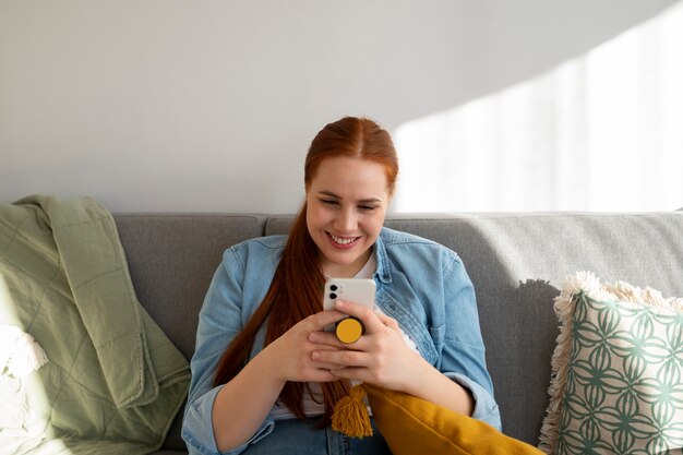 Portrait of woman using her smartphone at home on couch by holding from pop socket