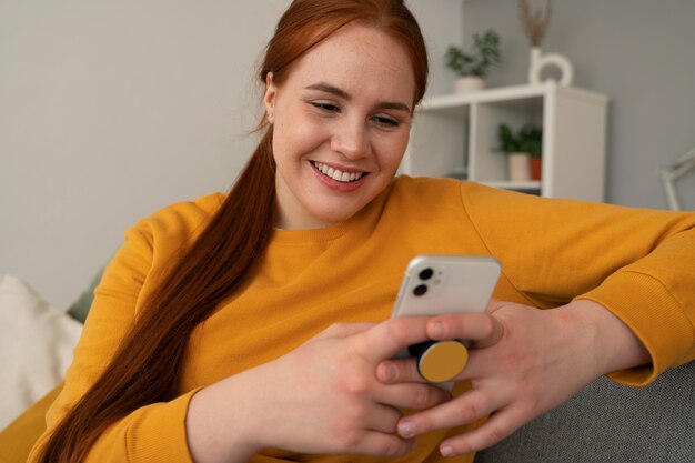 Portrait of woman using her smartphone at home on couch by holding from pop socket