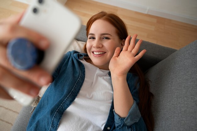 Portrait of woman using her smartphone at home on couch by holding from pop socket