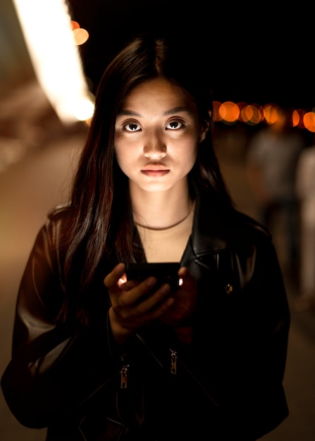 Portrait of woman using smartphone at night in the city lights