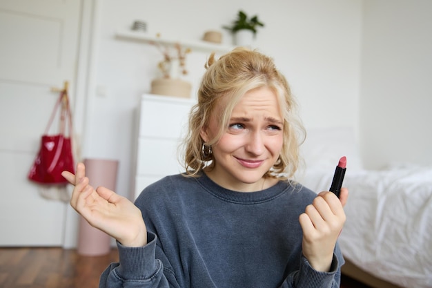 Portrait of woman vlogger looking disappointed showing lipstick and shrugging shoulders recording