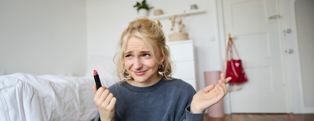 Portrait of woman vlogger looking disappointed showing lipstick and shrugging shoulders recording