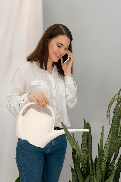 Portrait woman watering plant while talking on mobile