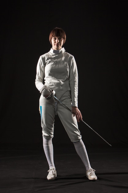 Free photo the portrait of woman wearing white fencing costume on black