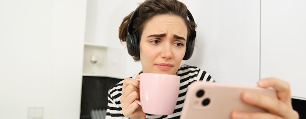 Free Photo portrait of woman with sad face watching something on mobile phone social media app drinking tea