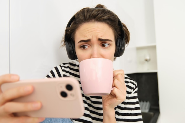 Free Photo portrait of woman with sad and worried face watching intense tv series on smartphone app drinking