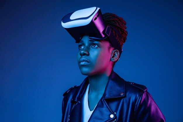 Portrait of young african-american woman's playing in VR-glasses in neon light on blue.