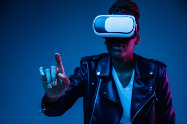 Portrait of young african-american woman's playing in VR-glasses in neon light on blue.