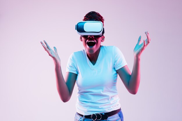 Portrait of young african-american woman's playing in VR-glasses in neon light on gradient background