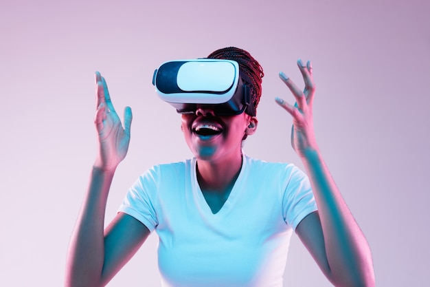 Portrait of young african-american woman's playing in VR-glasses in neon light on gradient background