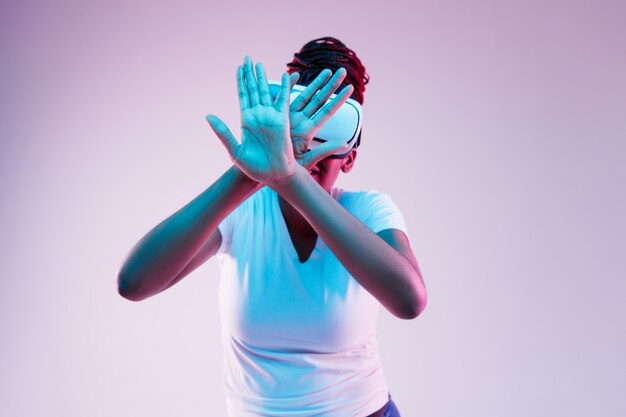 Portrait of young african-american woman's playing in VR-glasses in neon light on gradient background