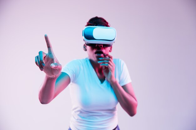 Portrait of young african-american woman's playing in VR-glasses in neon light on gradient.