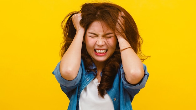 Portrait of young Asian lady with negative expression, excited screaming, crying emotional angry in casual clothing and looking at the camera over yellow wall. Facial expression concept.