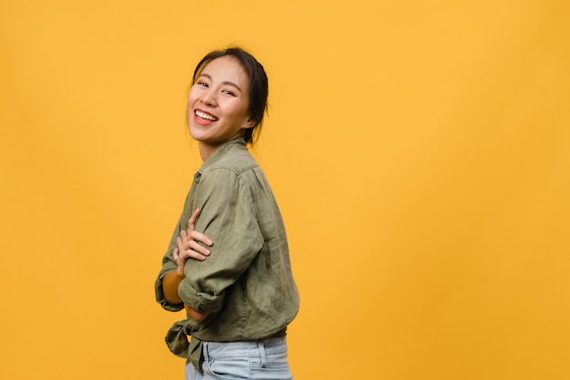 Portrait of young Asian lady with positive expression, arms crossed, smile broadly, dressed in casual clothing  over yellow wall. Happy adorable glad woman rejoices success.