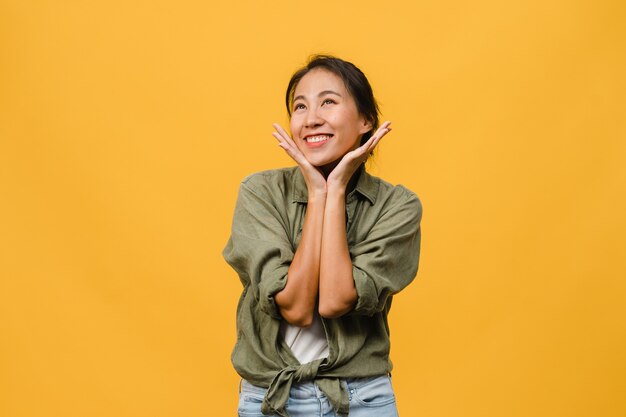 Portrait of young Asian lady with positive expression, smile broadly, dressed in casual clothing over yellow wall. Happy adorable glad woman rejoices success. Facial expression concept.