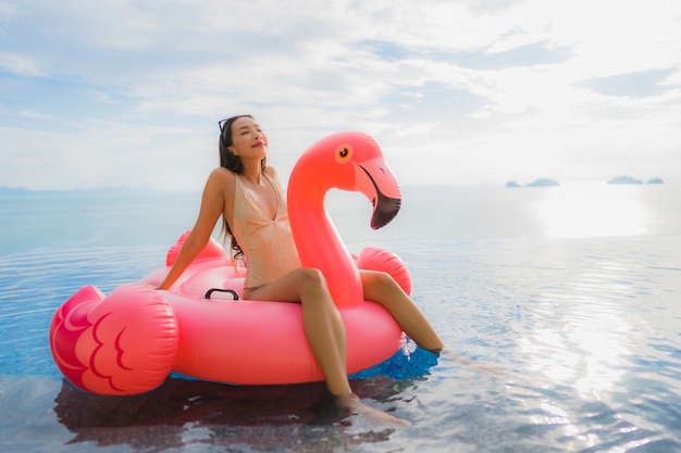 Portrait young asian woman on inflatable float flamingo around outdoor swimming pool in hotel resort