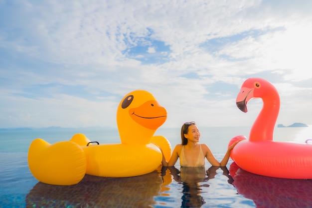 Free Photo portrait young asian woman on inflatable float yellow duck and pink flamingo around outdoor swimming pool in hotel and resort