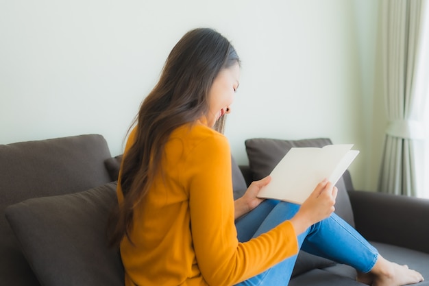 Portrait young asian woman read book on sofa chair with pillow in living room