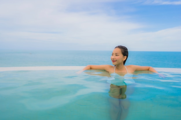 Portrait young asian woman relax smile happy around outdoor swimming pool in hotel resort with sea ocean view