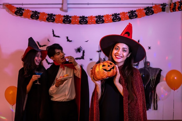 Portrait of young Asian woman smiling in Halloween costumer as witch in party pumpkin or Jack O Lantern looking at camera