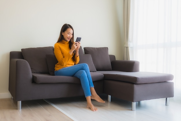 Portrait young asian woman using smart mobile phone on sofa with pillow in living room