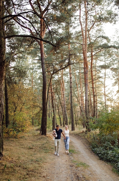 Free photo portrait of young attractive family with little baby son, posing in beautiful autumn pine forest at sunny day. handsome man and  his pretty brunette wife