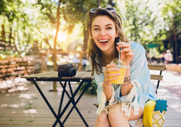 Portrait of young attractive stylish woman sitting in cafe, smiling sincerely, drinking juice smoothy, healthy lifestyle, street boho style, fashionable accessories, laughing, happy emotion, sunny