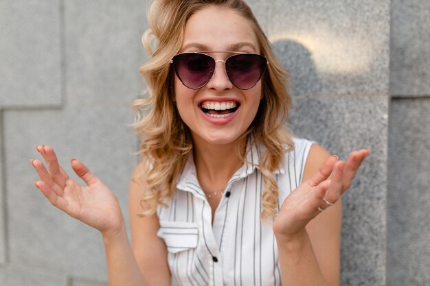 Portrait of young attractive stylish woman smiling  walking in city street in summer fashion style dress wearing sunglasses candid smile