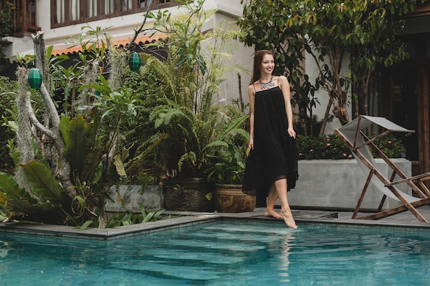 Free photo portrait of young attractive woman in elegant dress, straw hat, summer style, fashion trend, vacation, smiling, stylish accessories, sunglasses, posing on tropical villa on bali