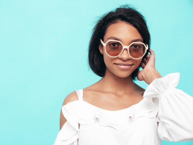 Free photo portrait of young beautiful black woman smiling model dressed in summer jeans clothes sexy carefree female posing near blue wall in studio tanned and cheerful in sunglasses