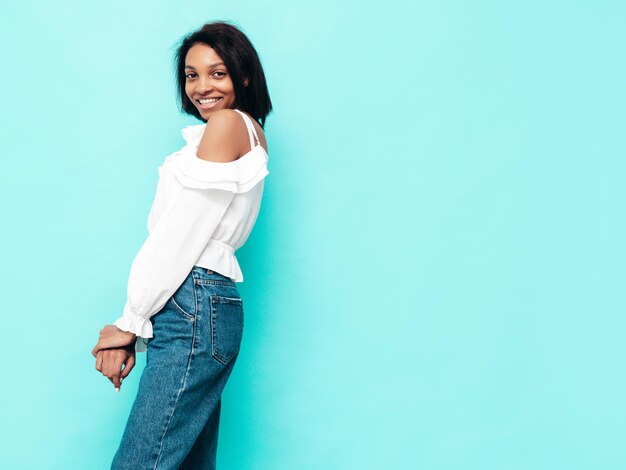 Portrait of young beautiful black woman Smiling model dressed in summer jeans clothes Sexy carefree female posing near blue wall in studio Tanned and cheerful