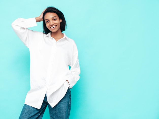 Portrait of young beautiful black woman Smiling model dressed in summer jeans clothes Sexy carefree female posing near blue wall in studio Tanned and cheerful