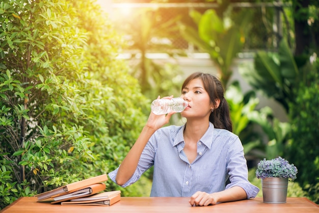 Portrait of young beautiful dark-haired woman wearing blue t-shirt drinking water at summer green park.