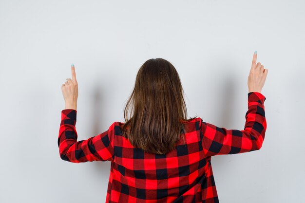 Portrait of young beautiful female pointing up in casual shirt and looking curious back view