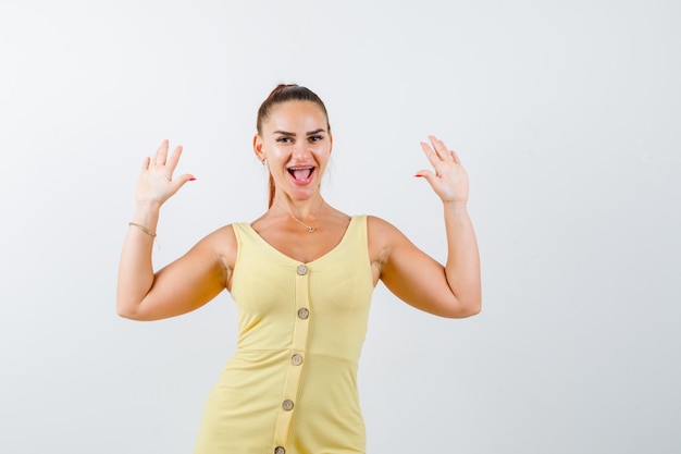 Portrait of young beautiful female showing surrender gesture in dress and looking merry front view